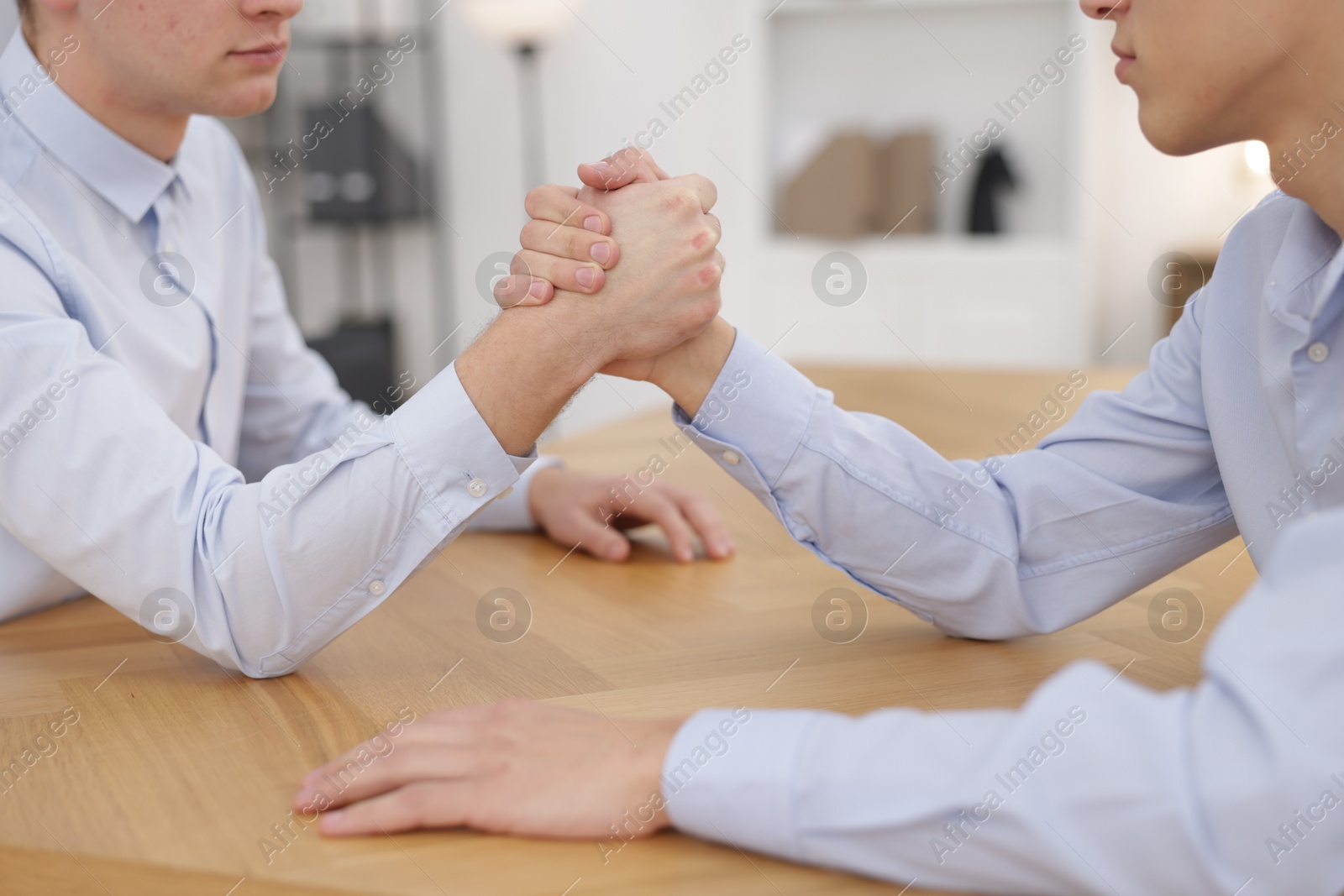 Photo of Competition concept. Businessmen arm wrestling at table in office, closeup