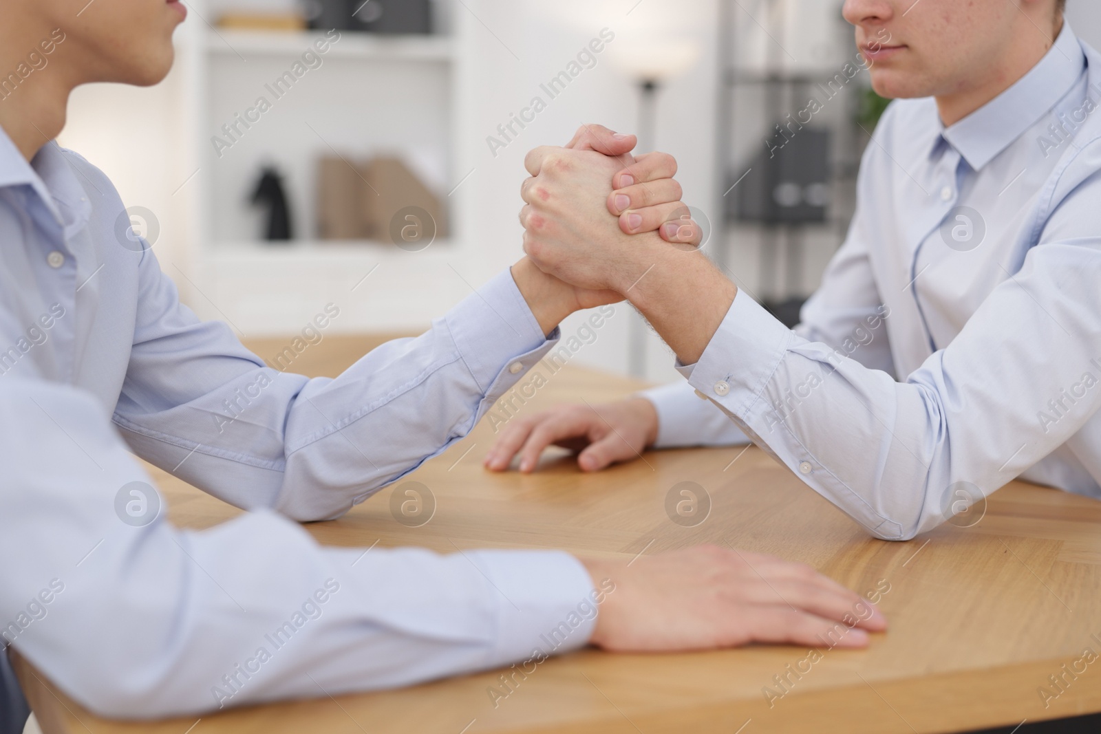 Photo of Competition concept. Businessmen arm wrestling at table in office, closeup