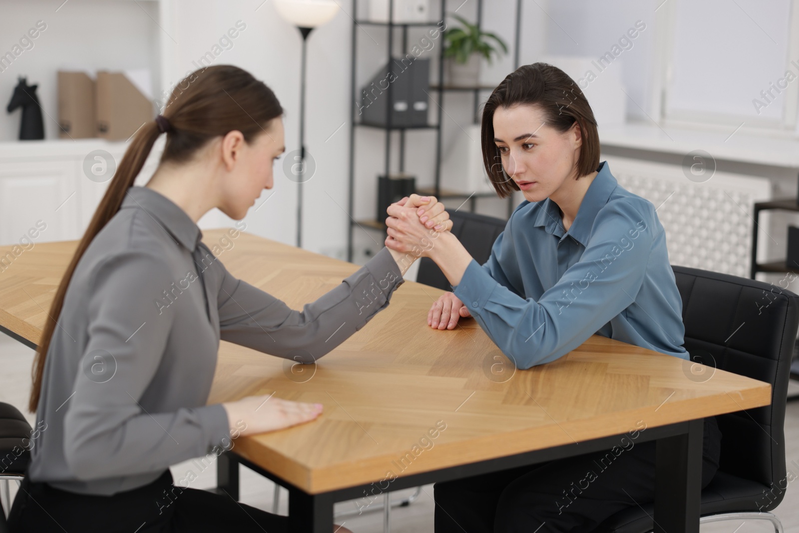 Photo of Competition concept. Businesswomen arm wrestling at table in office