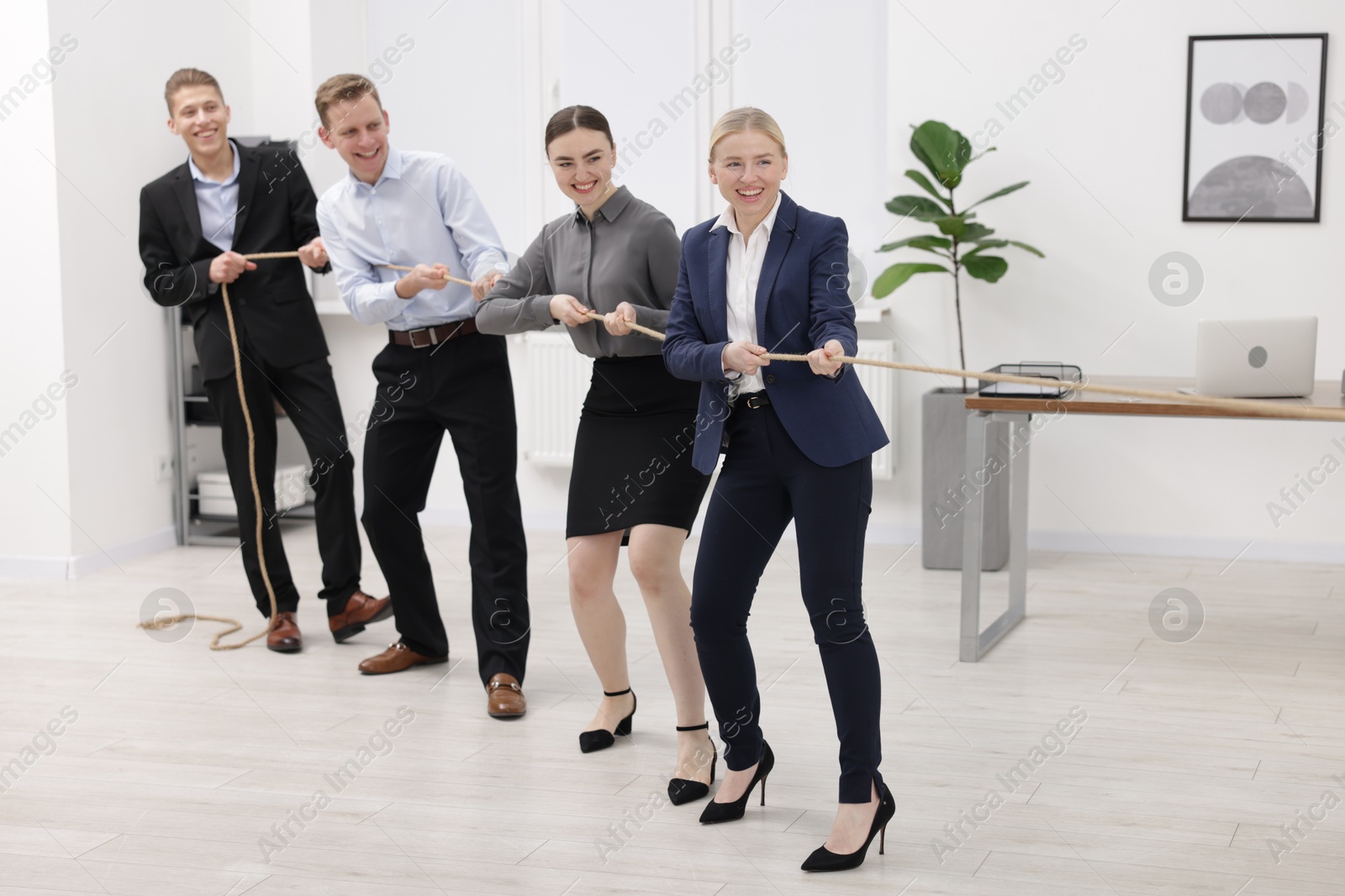 Photo of Competition concept. Group of happy businesspeople pulling rope in office