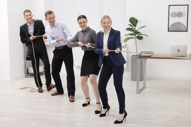 Competition concept. Group of happy businesspeople pulling rope in office