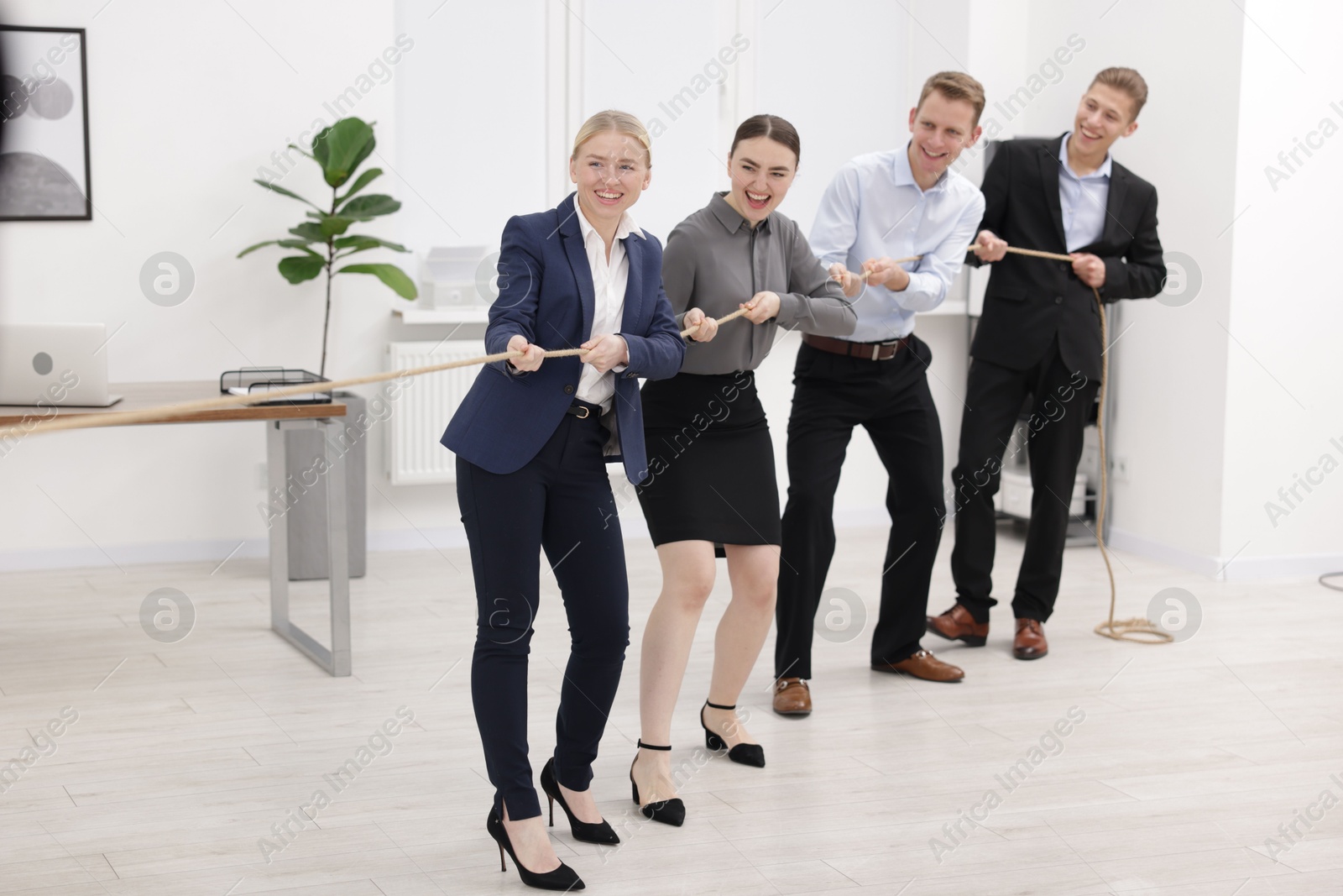 Photo of Competition concept. Group of happy businesspeople pulling rope in office