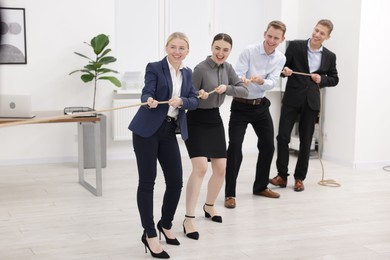 Photo of Competition concept. Group of happy businesspeople pulling rope in office