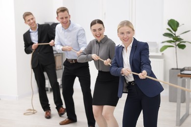 Photo of Competition concept. Group of happy businesspeople pulling rope in office