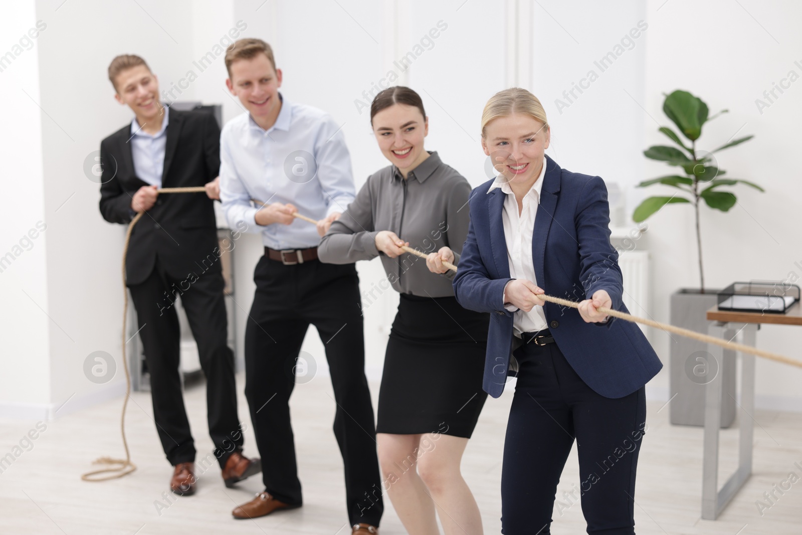 Photo of Competition concept. Group of happy businesspeople pulling rope in office