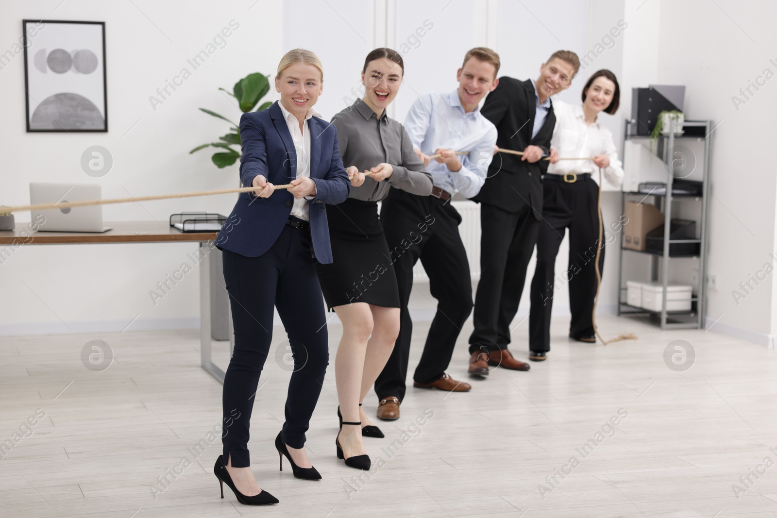 Photo of Competition concept. Group of happy businesspeople pulling rope in office