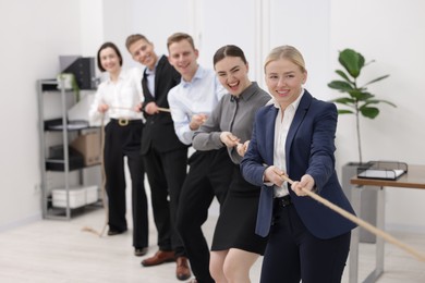 Photo of Competition concept. Group of happy businesspeople pulling rope in office