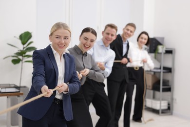 Photo of Competition concept. Group of happy businesspeople pulling rope in office