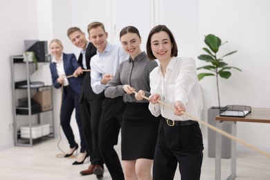 Photo of Competition concept. Group of happy businesspeople pulling rope in office