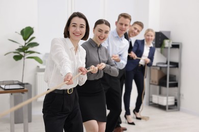 Photo of Competition concept. Group of happy businesspeople pulling rope in office