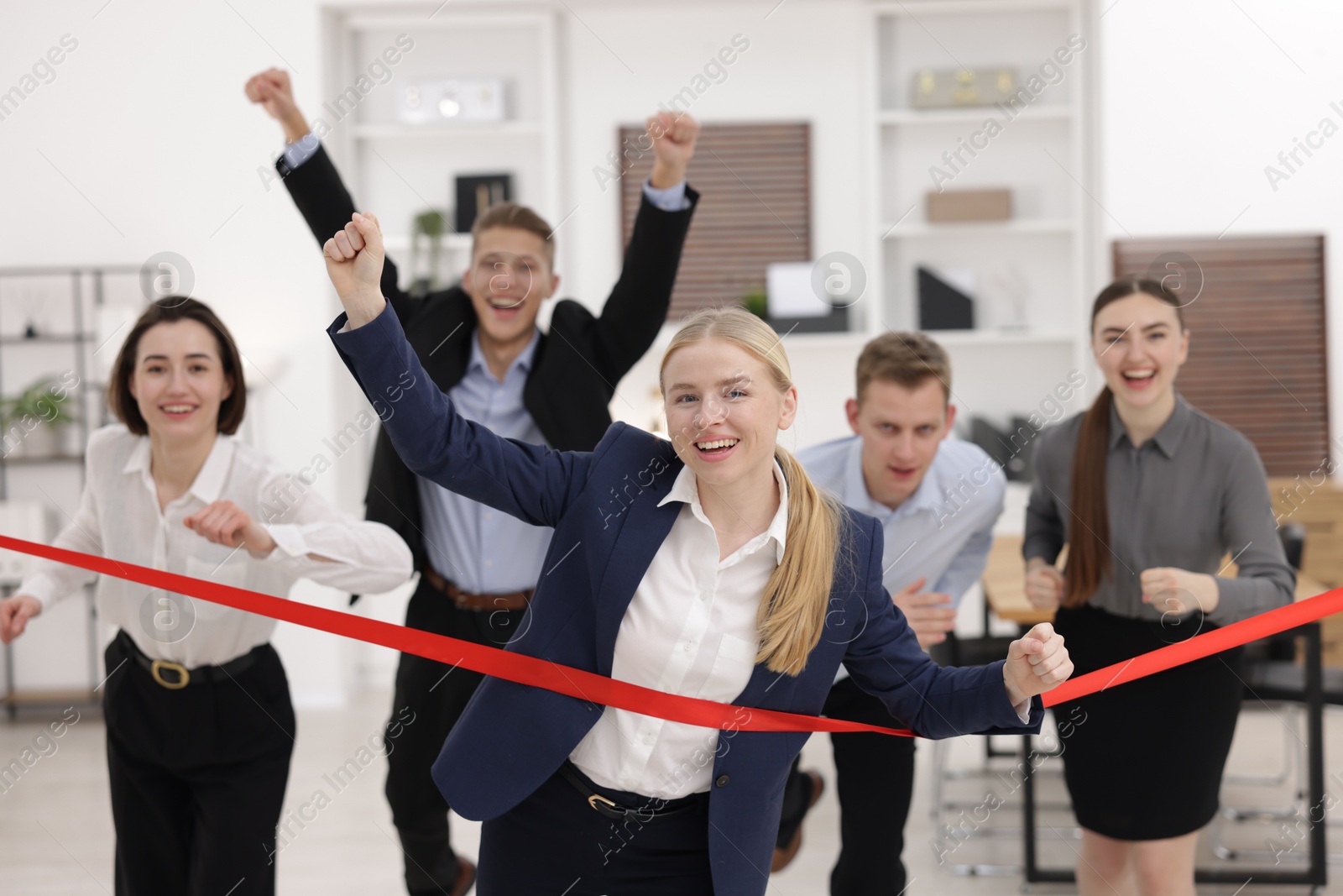 Photo of Competition concept. Happy businesswoman crossing red finish line ahead of her colleagues in office