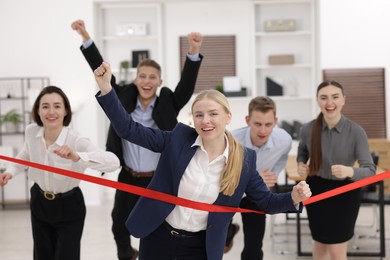 Competition concept. Happy businesswoman crossing red finish line ahead of her colleagues in office