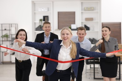 Competition concept. Happy businesswoman crossing red finish line ahead of her colleagues in office