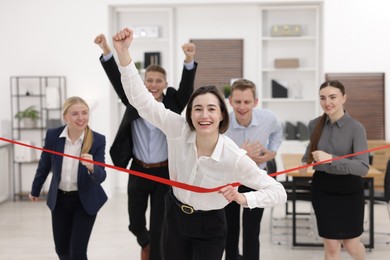 Photo of Competition concept. Happy businesswoman crossing red finish line ahead of her colleagues in office