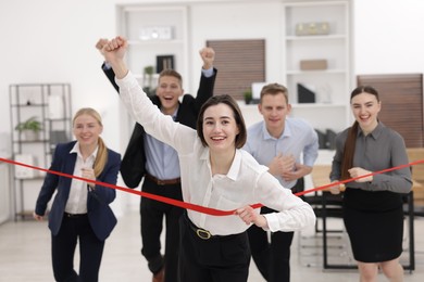 Photo of Competition concept. Happy businesswoman crossing red finish line ahead of her colleagues in office