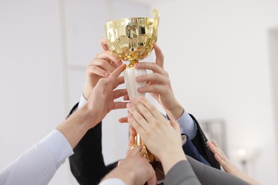 Photo of Competition concept. Group of businesspeople with golden trophy in office, closeup