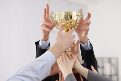 Photo of Competition concept. Group of businesspeople with golden trophy in office, closeup