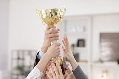 Photo of Competition concept. Group of businesspeople with golden trophy in office, closeup