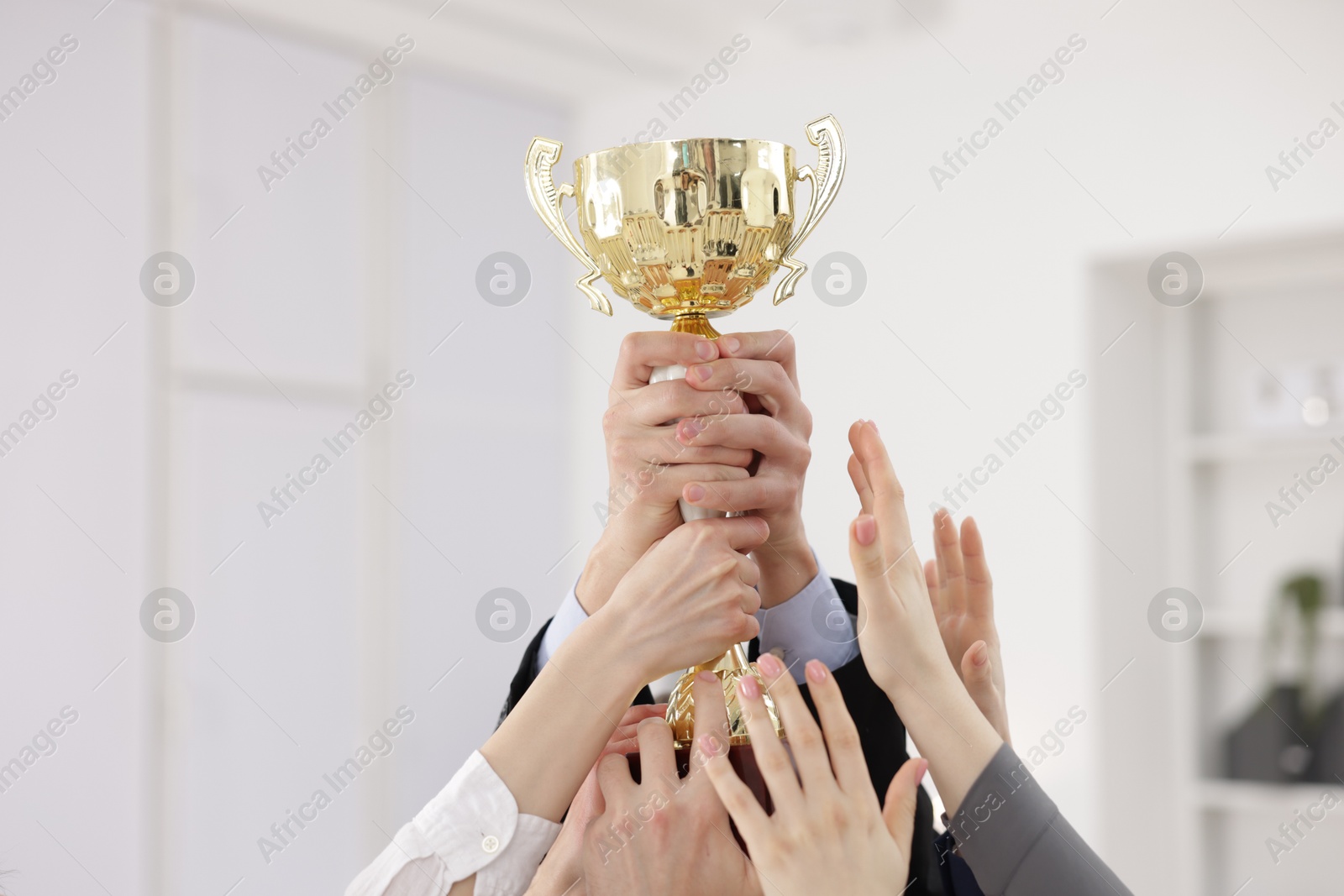 Photo of Competition concept. Group of businesspeople with golden trophy in office, closeup