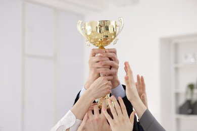 Photo of Competition concept. Group of businesspeople with golden trophy in office, closeup