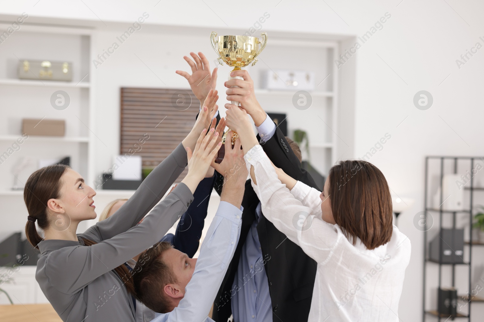 Photo of Competition concept. Group of businesspeople with golden trophy in office