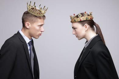 Business competition. Colleagues in golden crowns looking at each other on grey background