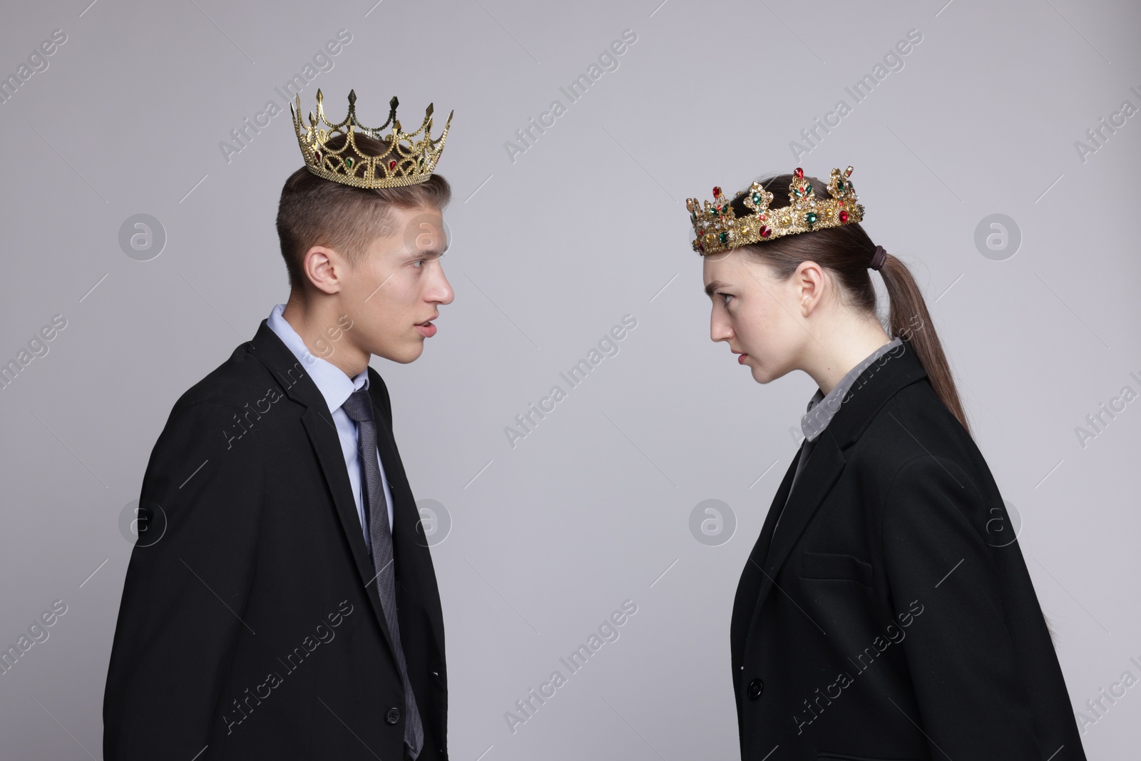 Photo of Business competition. Colleagues in golden crowns looking at each other on grey background