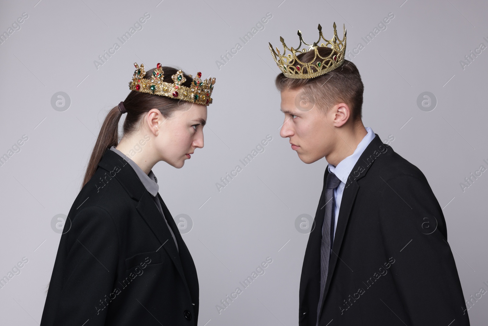 Photo of Business competition. Colleagues in golden crowns looking at each other on grey background