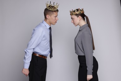 Business competition. Colleagues in golden crowns looking at each other on grey background