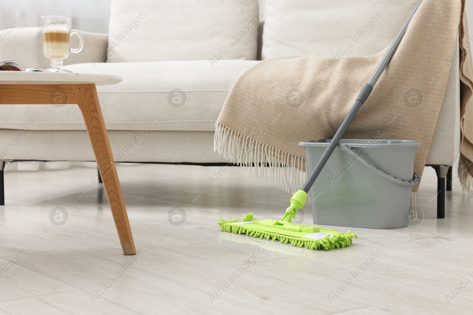 Photo of Microfiber mop and bucket near sofa indoors