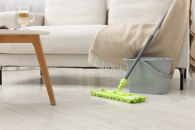 Photo of Microfiber mop and bucket near sofa indoors