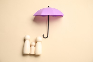 Photo of Human figures under umbrella on beige background, top view. Insurance concept