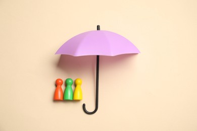 Photo of Human figures under umbrella on beige background, top view. Insurance concept