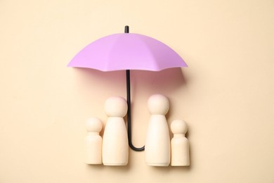 Photo of Human figures under umbrella on beige background, top view. Insurance concept