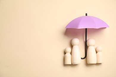 Photo of Human figures under umbrella on beige background, top view with space for text. Insurance concept