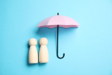 Photo of Human figures under umbrella on light blue background, top view. Insurance concept