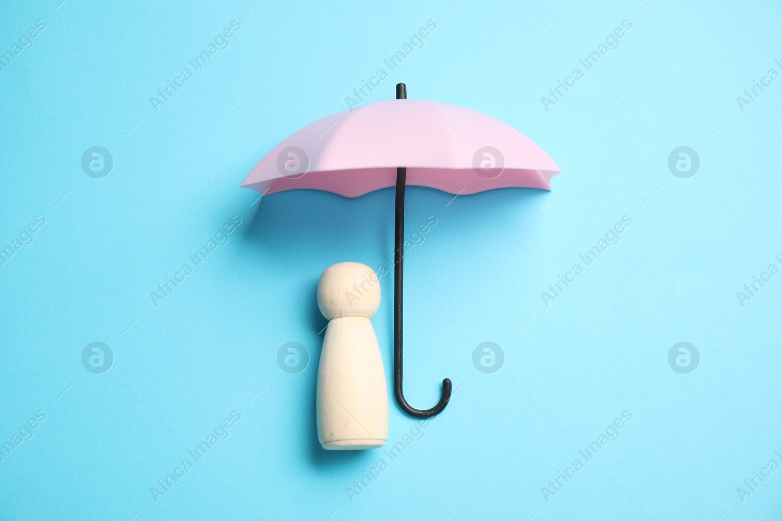 Photo of Human figure under umbrella on light blue background, top view. Insurance concept