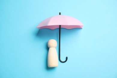 Photo of Human figure under umbrella on light blue background, top view. Insurance concept