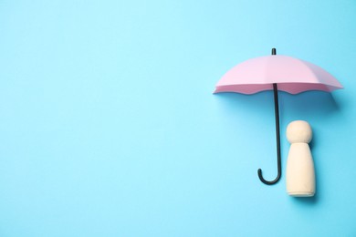 Photo of Human figure under umbrella on light blue background, top view with space for text. Insurance concept