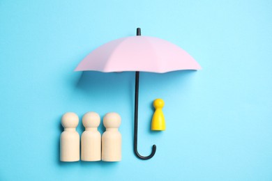 Photo of Human figures under umbrella on light blue background, top view. Insurance concept