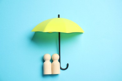 Photo of Human figures under umbrella on light blue background, top view. Insurance concept