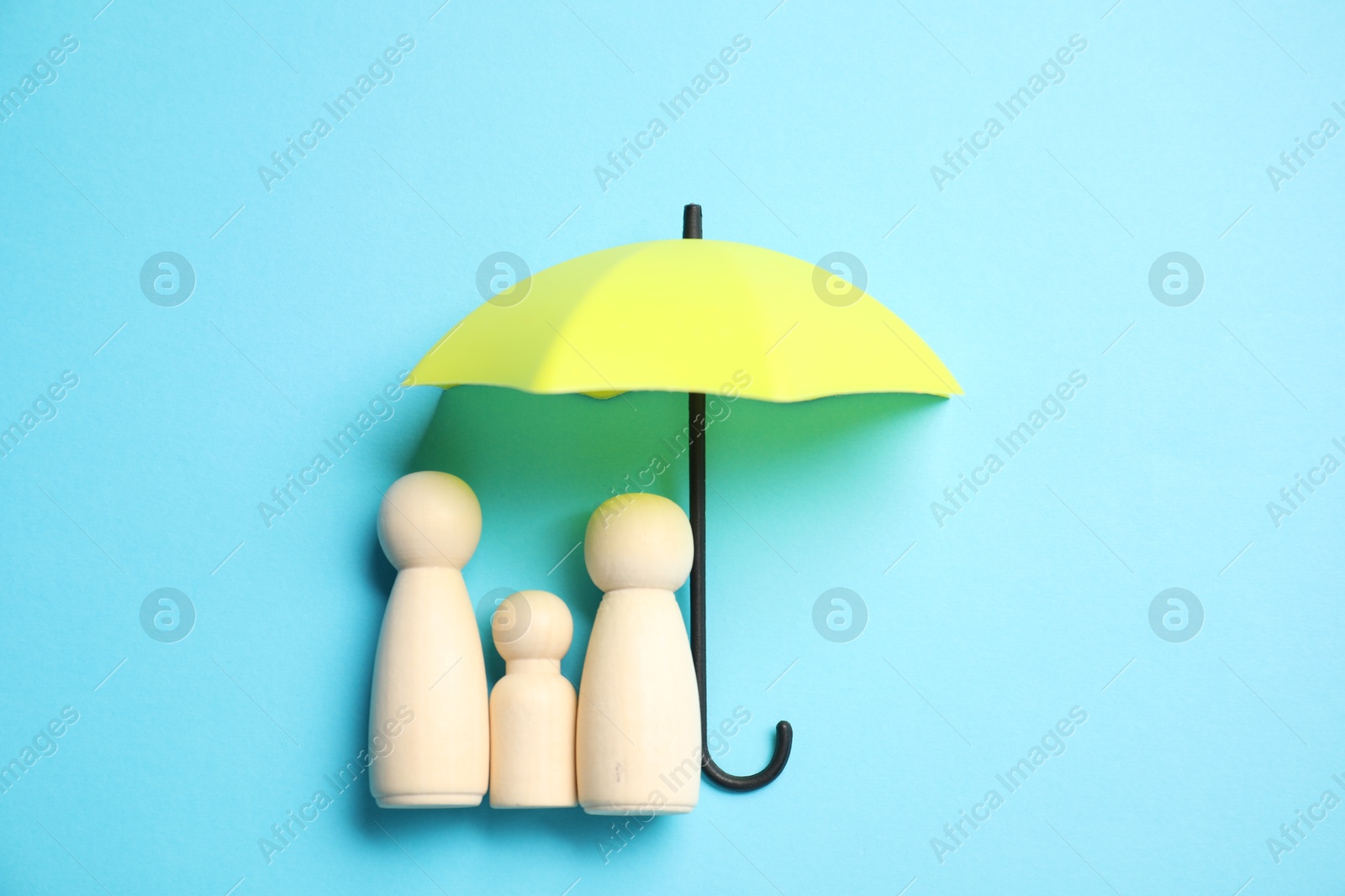 Photo of Human figures under umbrella on light blue background, top view. Insurance concept