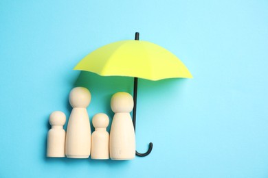 Photo of Human figures under umbrella on light blue background, top view. Insurance concept