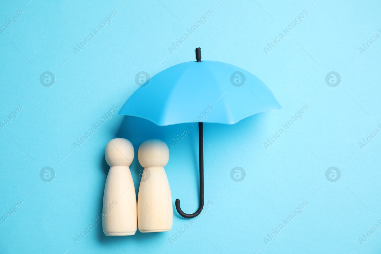 Photo of Human figures under umbrella on light blue background, top view. Insurance concept