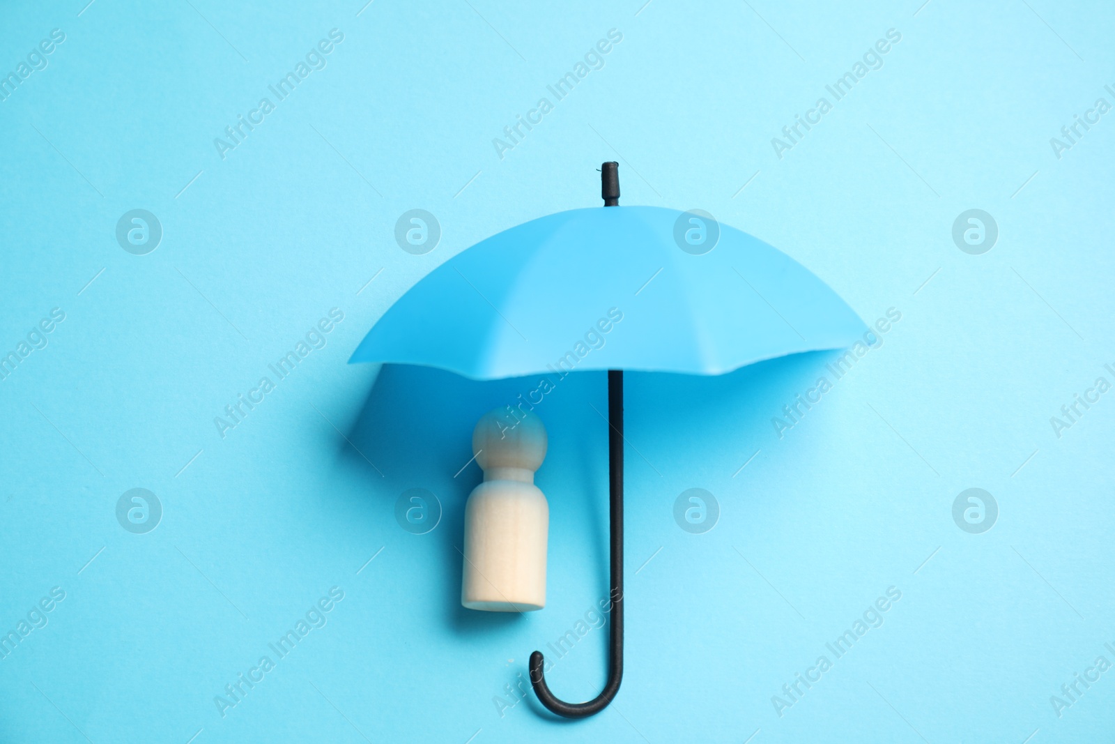 Photo of Human figure under umbrella on light blue background, top view. Insurance concept