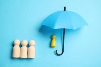 Photo of Human figures under umbrella on light blue background, top view. Insurance concept