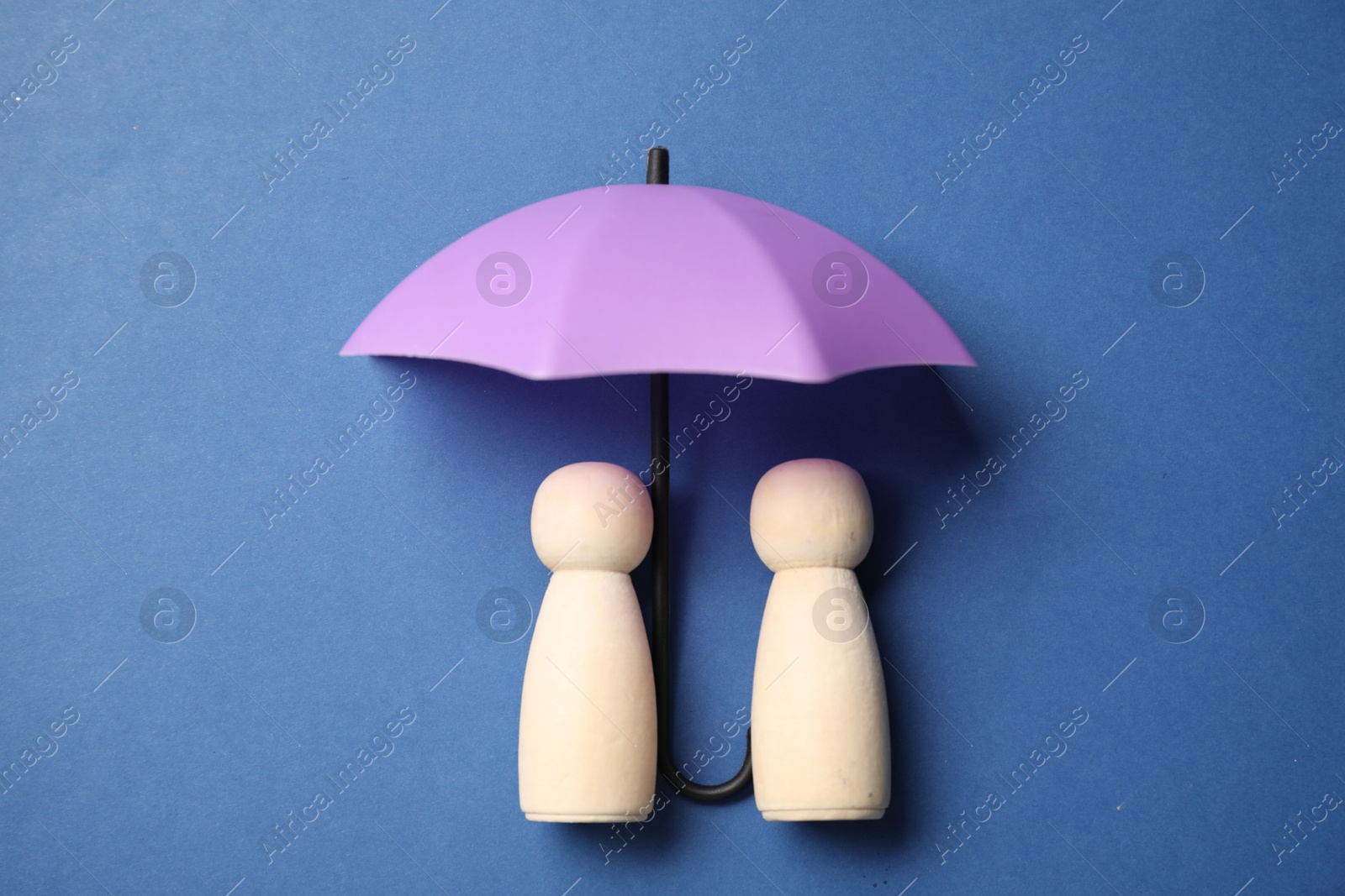 Photo of Human figures under umbrella on blue background, top view. Insurance concept