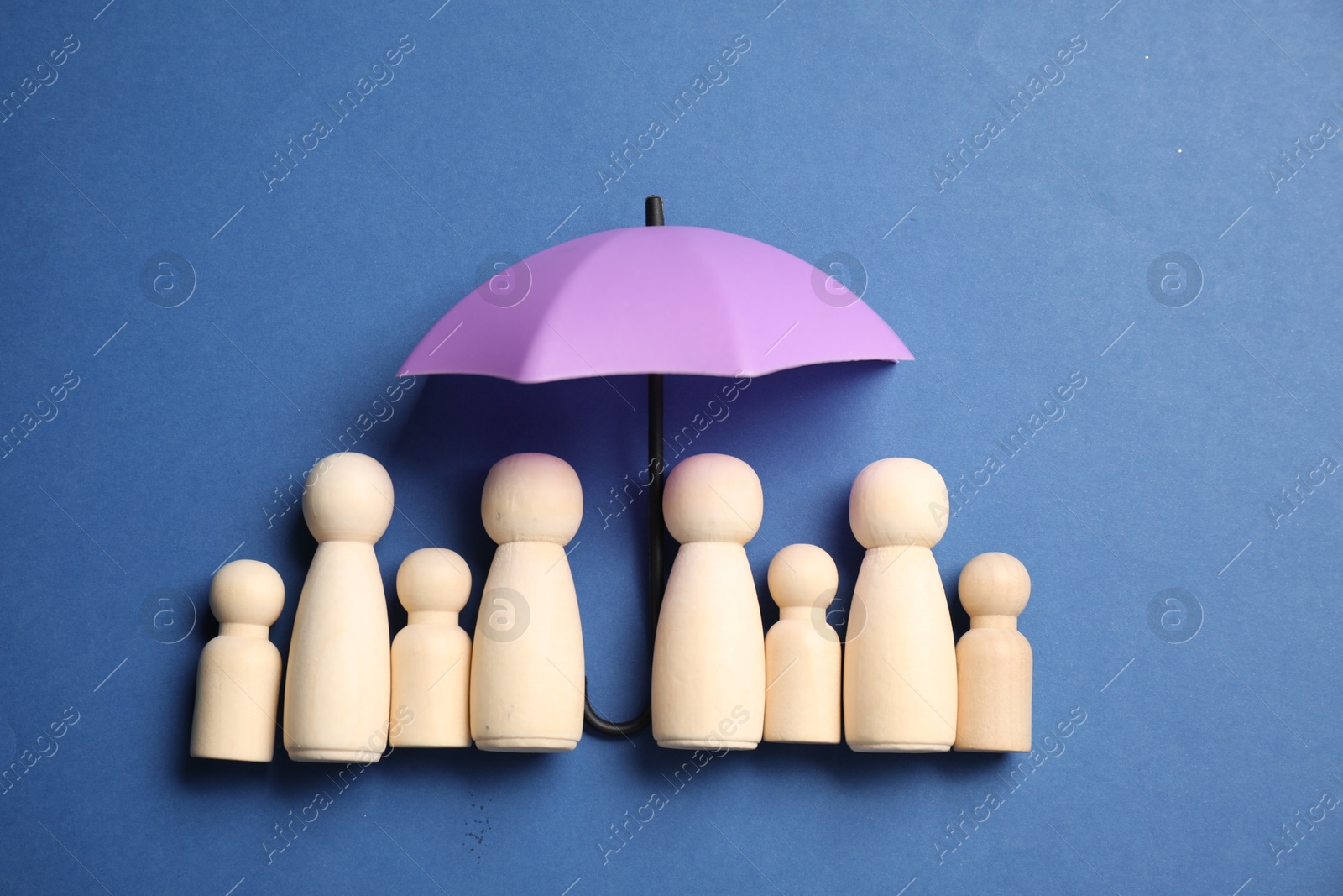 Photo of Human figures under umbrella on blue background, top view. Insurance concept