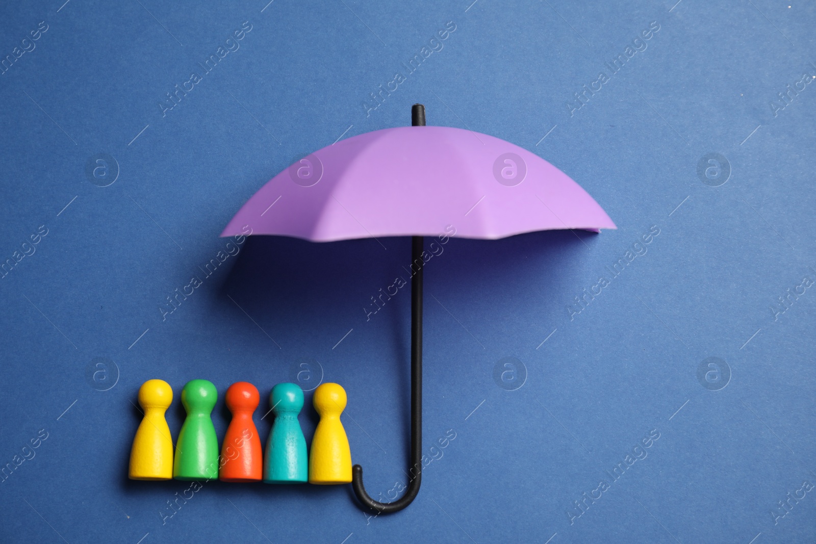 Photo of Human figures under umbrella on blue background, top view. Insurance concept