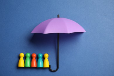 Photo of Human figures under umbrella on blue background, top view. Insurance concept